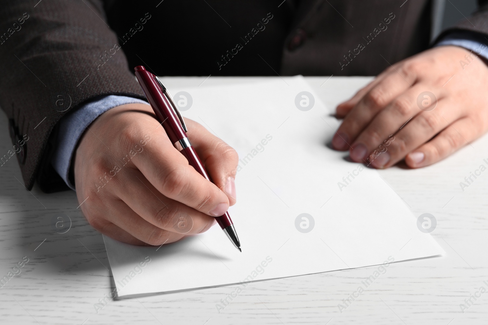 Photo of Man writing on sheet of paper with pen at white wooden table, closeup