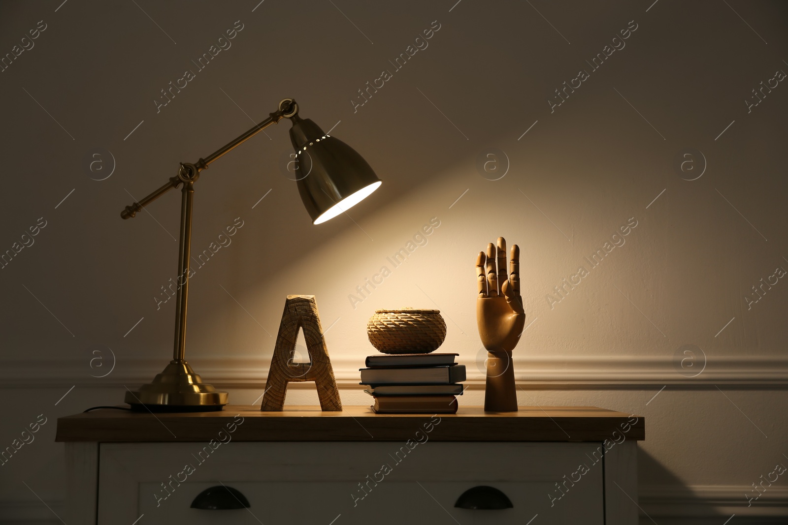 Photo of Wooden chest of drawers with books, decor and modern lamp near beige wall. Interior element