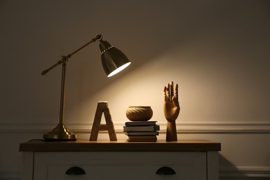 Wooden chest of drawers with books, decor and modern lamp near beige wall. Interior element