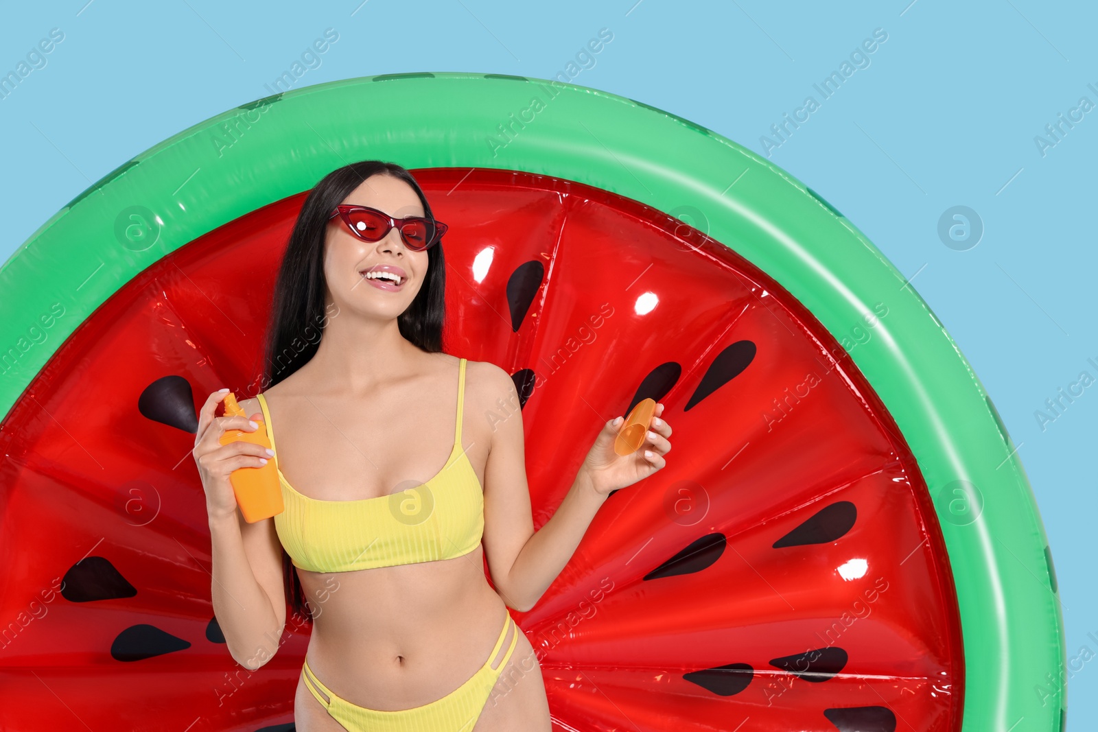 Photo of Young woman with sun protection cream near inflatable mattress against light blue background