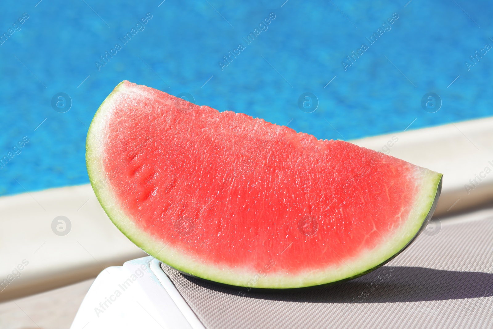 Photo of Slice of fresh juicy watermelon near swimming pool outdoors, closeup