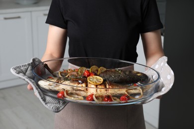 Woman holding baking tray with sea bass fish and garnish, closeup