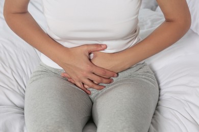 Photo of Young woman suffering from cystitis on bed, closeup