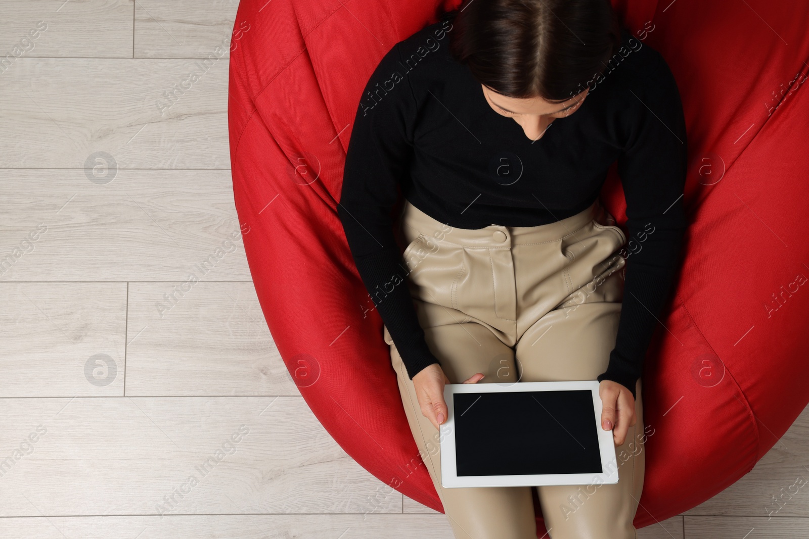 Photo of Woman working with tablet on beanbag chair, top view. Space for text