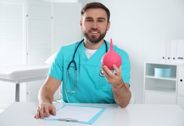 Doctor holding rubber enema at table in examination room