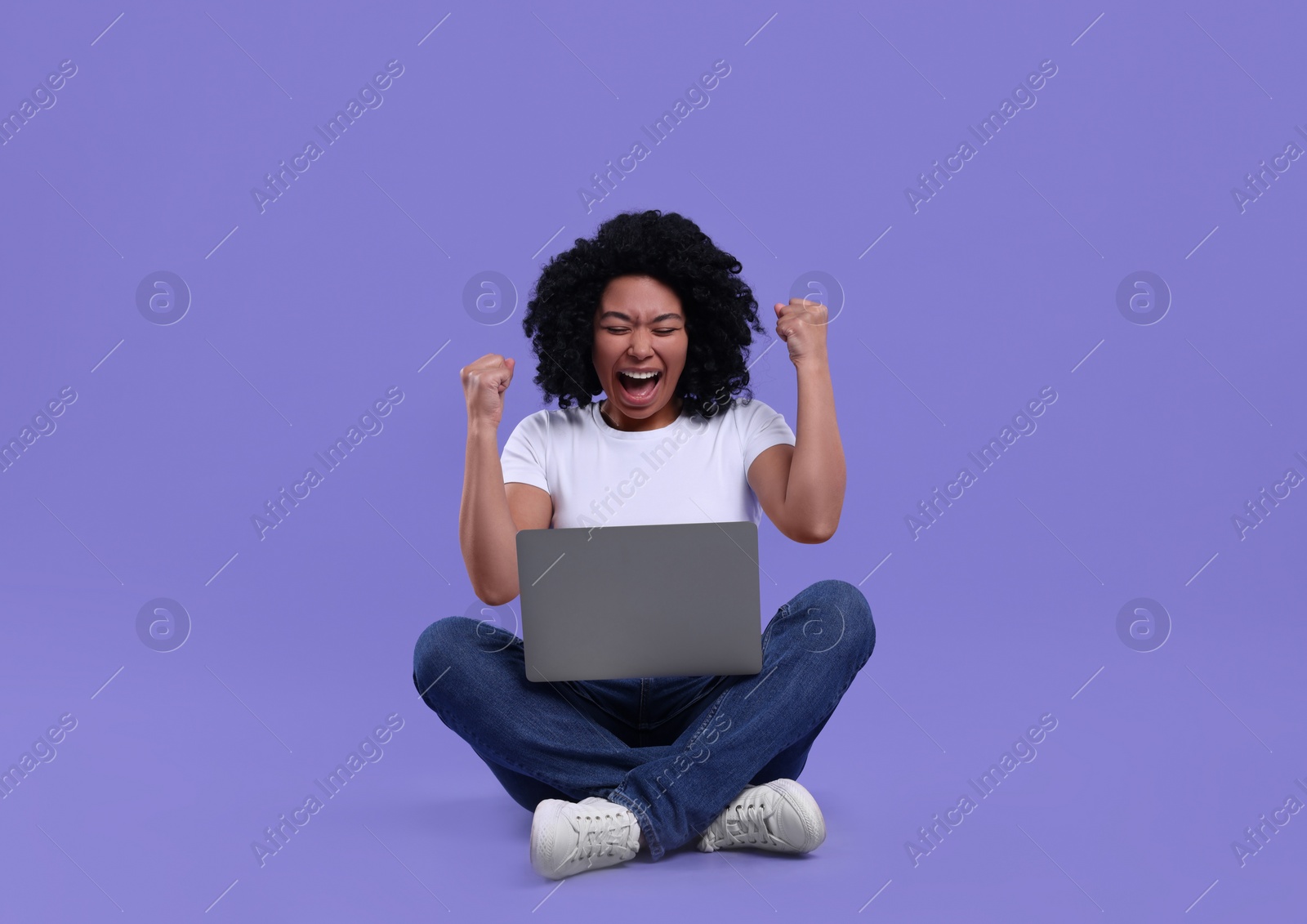 Photo of Emotional young woman using laptop on purple background