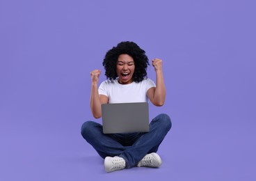 Emotional young woman using laptop on purple background