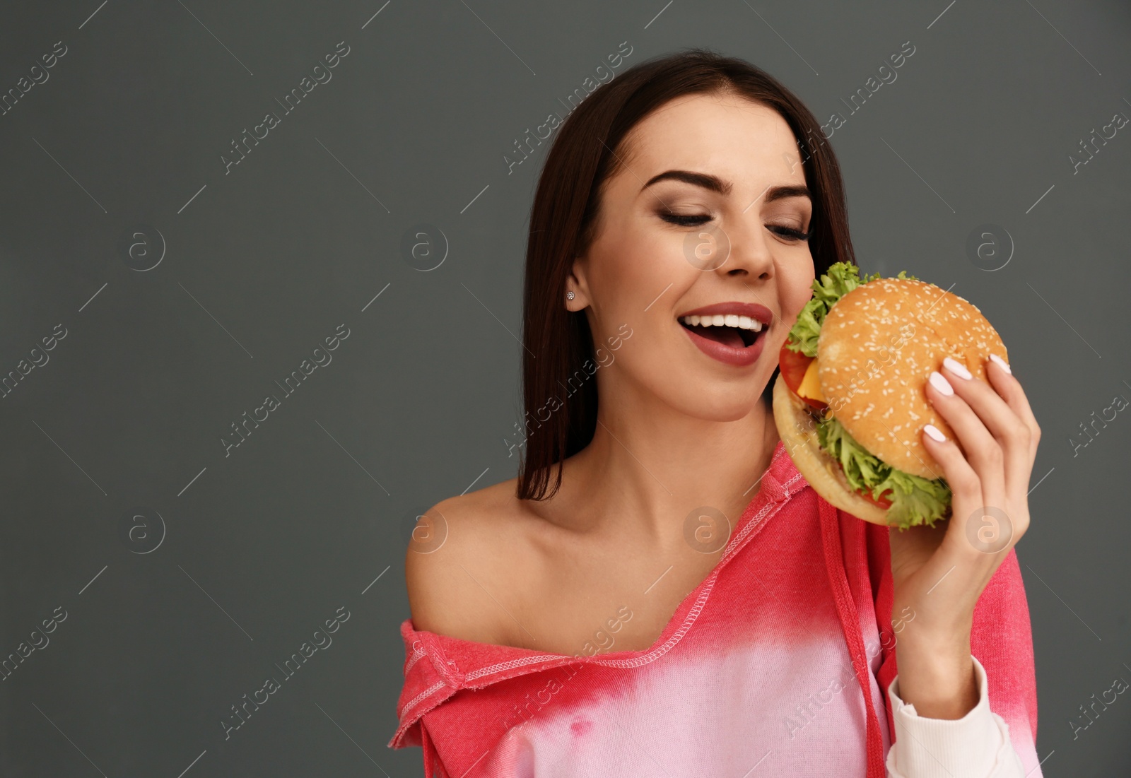 Photo of Young woman eating tasty burger on grey background. Space for text