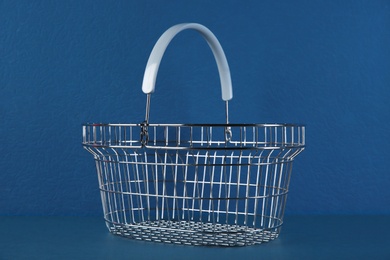 Photo of Empty metal shopping basket on blue background