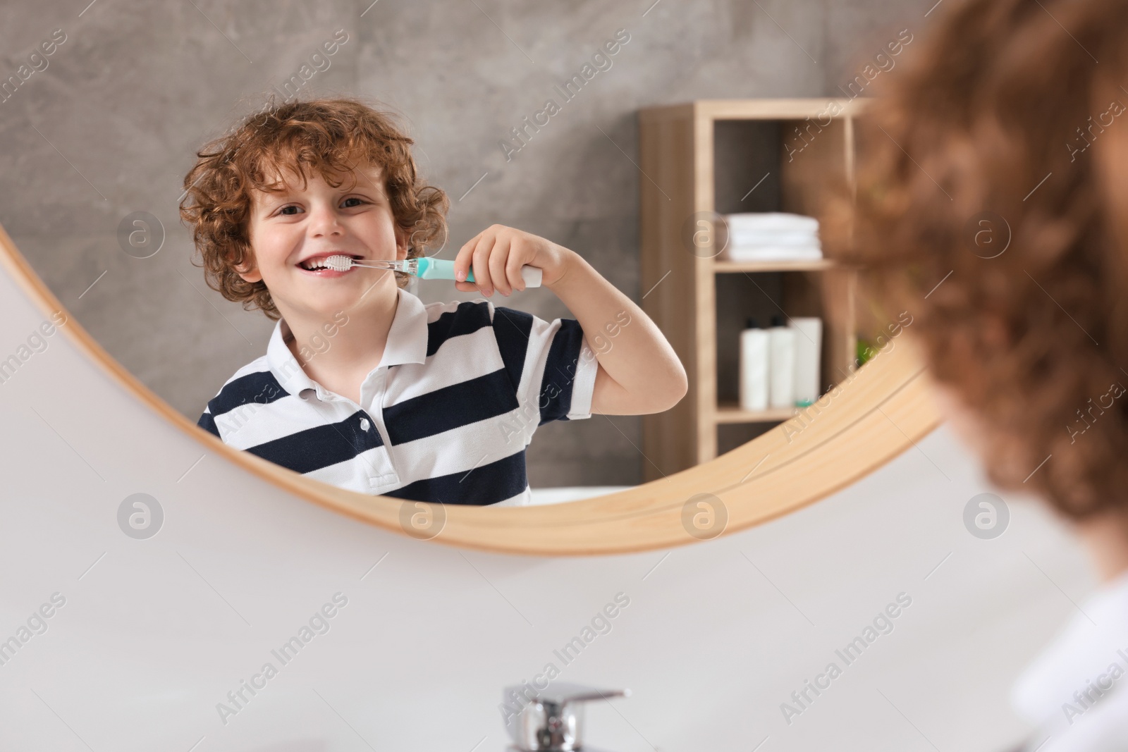 Photo of Cute little boy brushing his teeth with electric toothbrush near mirror in bathroom