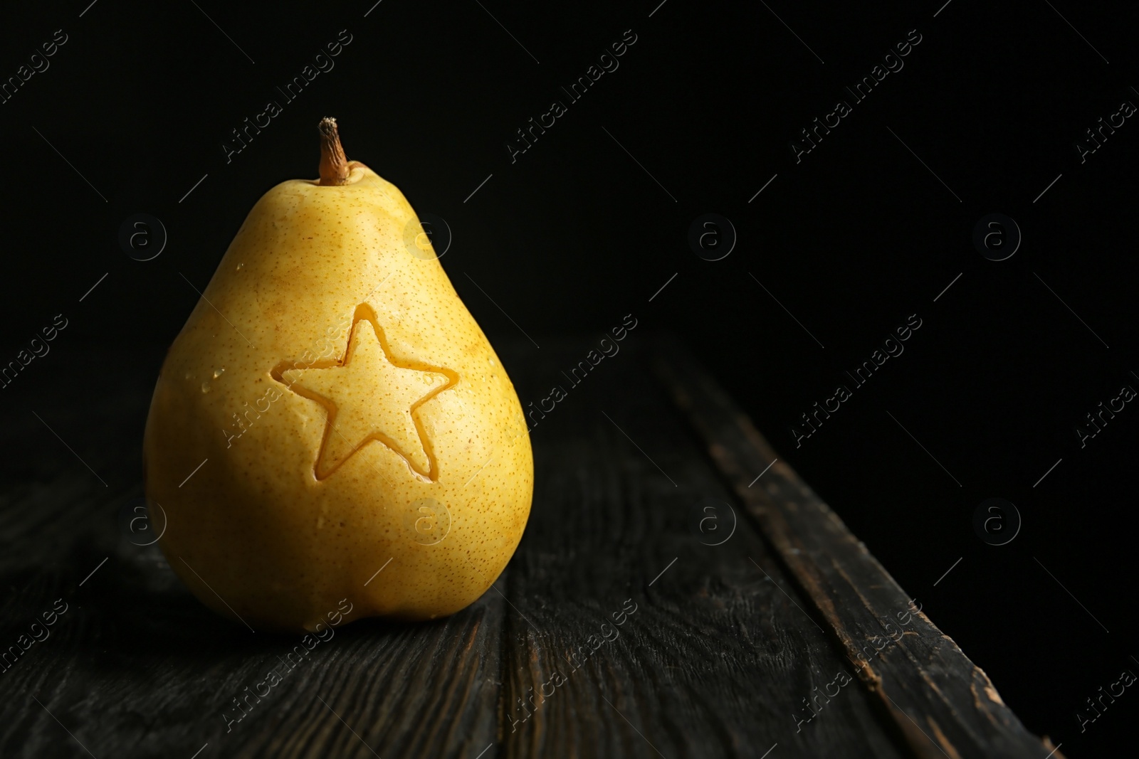 Photo of Ripe pear with carved star on wooden table against dark background. Space for text