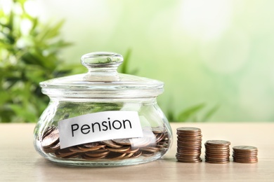 Glass jar with label PENSION and coins on wooden table. Space for text