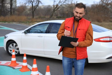 Photo of Instructor with clipboard near car on test track. Driving school