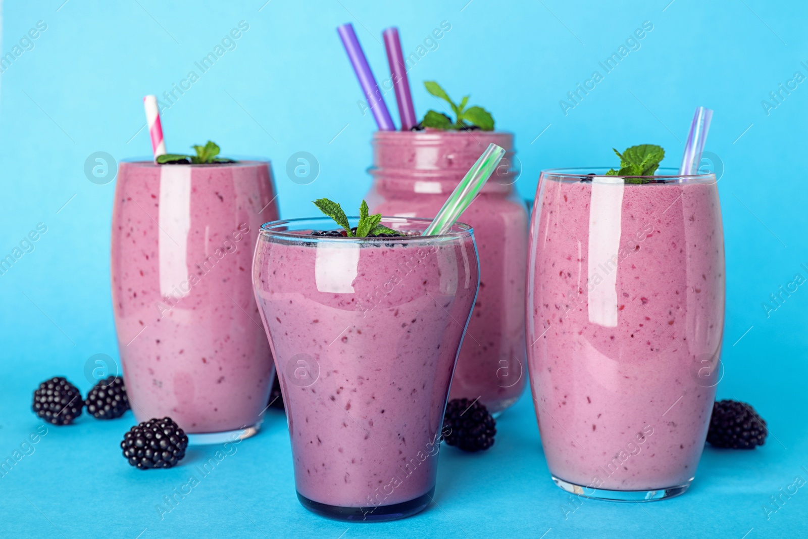 Photo of Glasses and mason jar with tasty blackberry smoothie on blue background