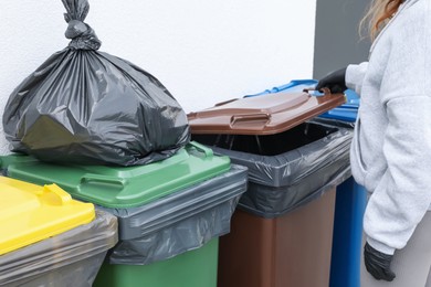 Photo of Woman opening bin to throw trash bag full of garbage outdoors, closeup. Recycling concept