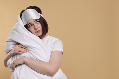 Photo of Unhappy young woman with sleep mask and pillow on beige background, space for text. Insomnia problem