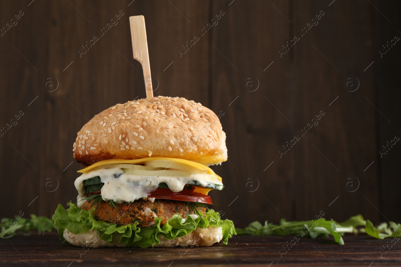 Photo of Delicious vegetarian burger and arugula on wooden table, space for text