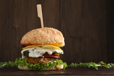 Photo of Delicious vegetarian burger and arugula on wooden table, space for text