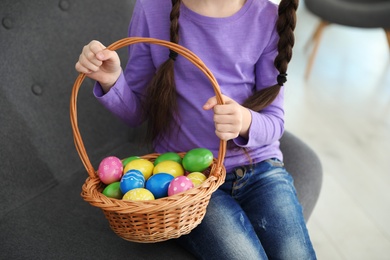 Photo of Little girl holding basket with Easter eggs at home, closeup