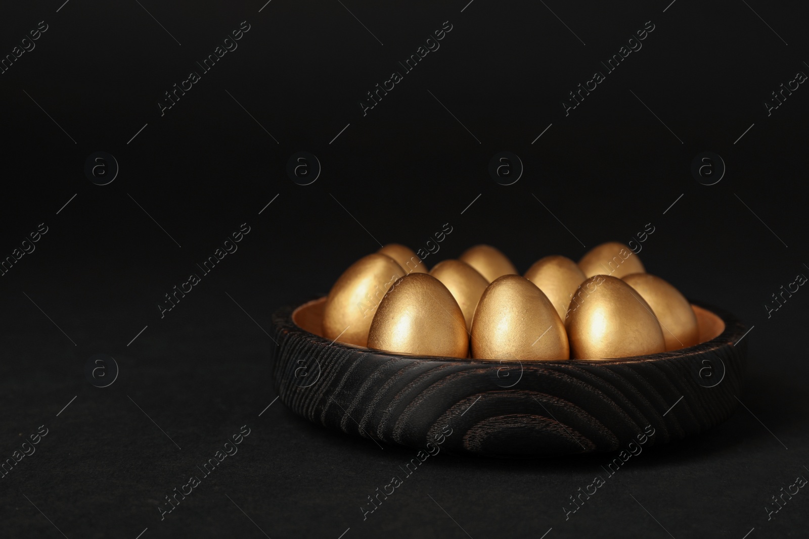 Photo of Shiny golden eggs on black background, space for text