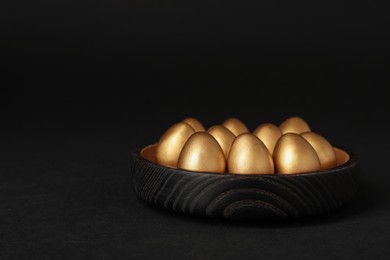 Shiny golden eggs on black background, space for text