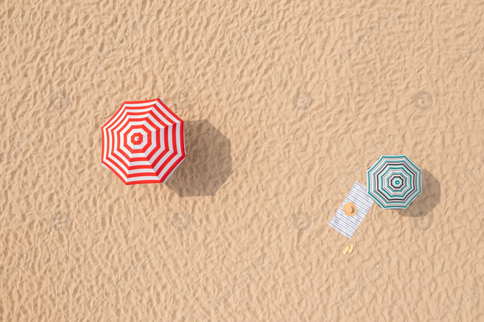 Image of Striped beach umbrellas, towel, hat and flip flops on sandy coast, aerial view