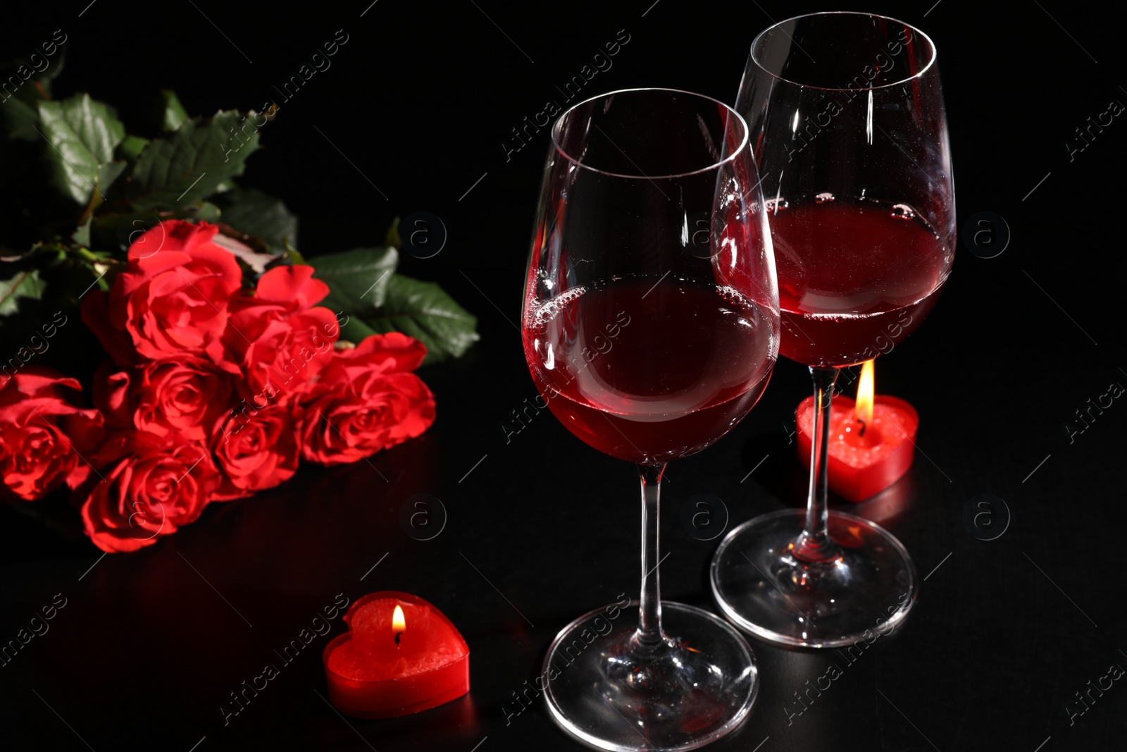 Photo of Glasses of wine, roses and heart shaped candles for romantic dinner on black table