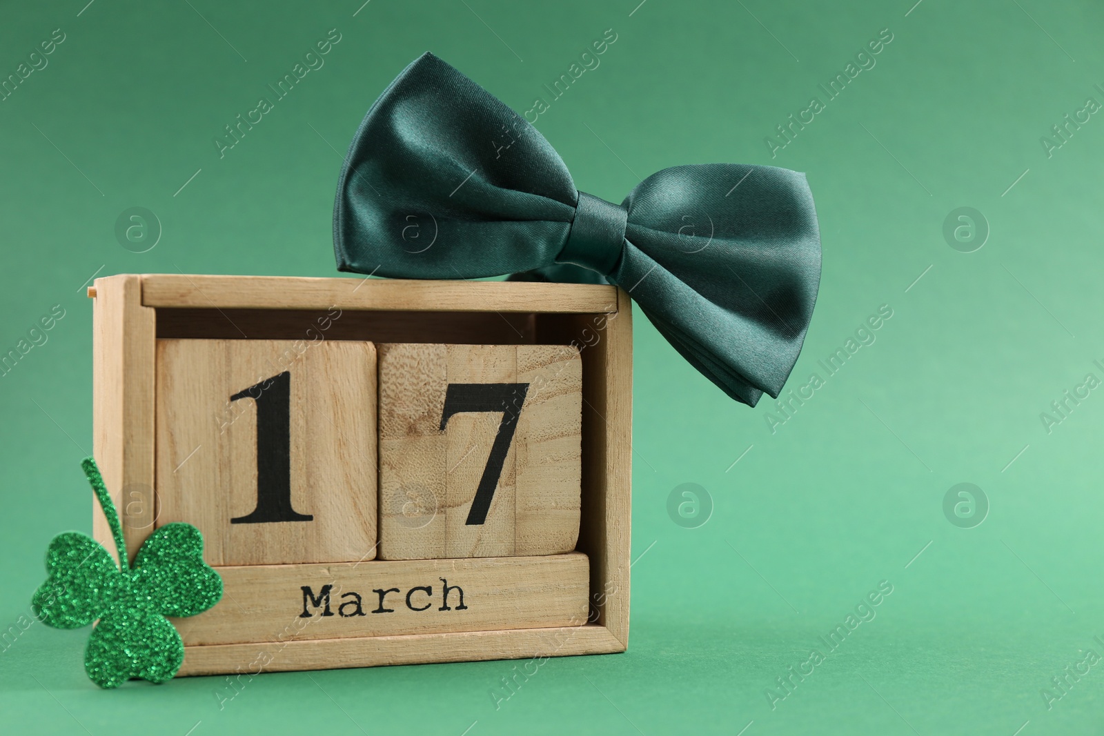 Photo of St. Patrick's day - 17th of March. Block calendar, bowtie and clover leaf on green background