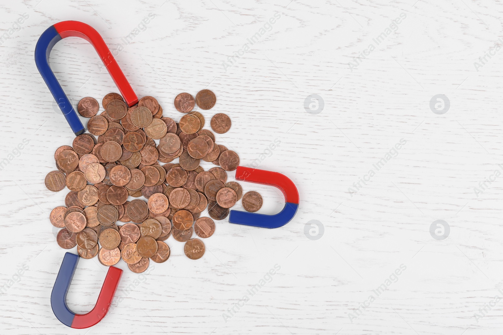 Photo of Magnets attracting coins on white wooden table, flat lay. Space for text