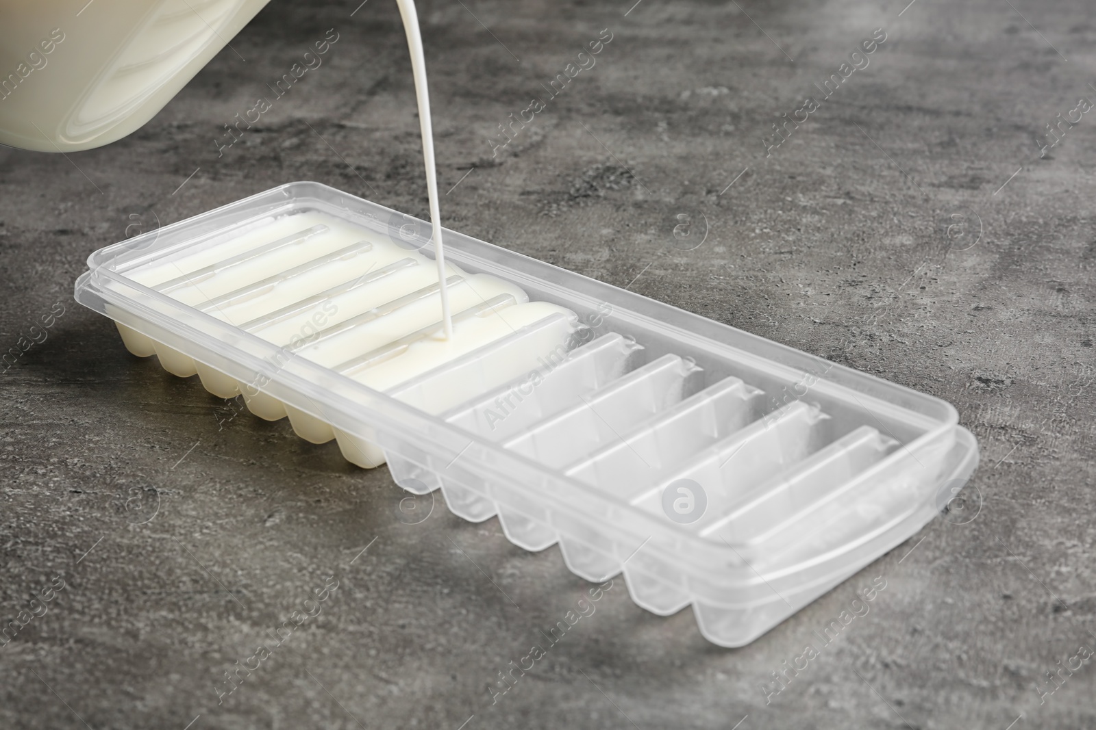 Photo of Pouring milk into ice cube tray on grey table