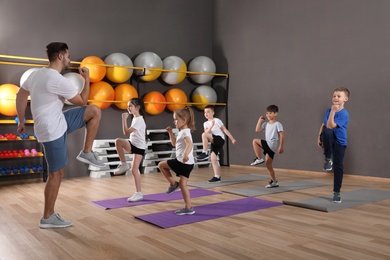 Cute little children and trainer doing physical exercise in school gym. Healthy lifestyle