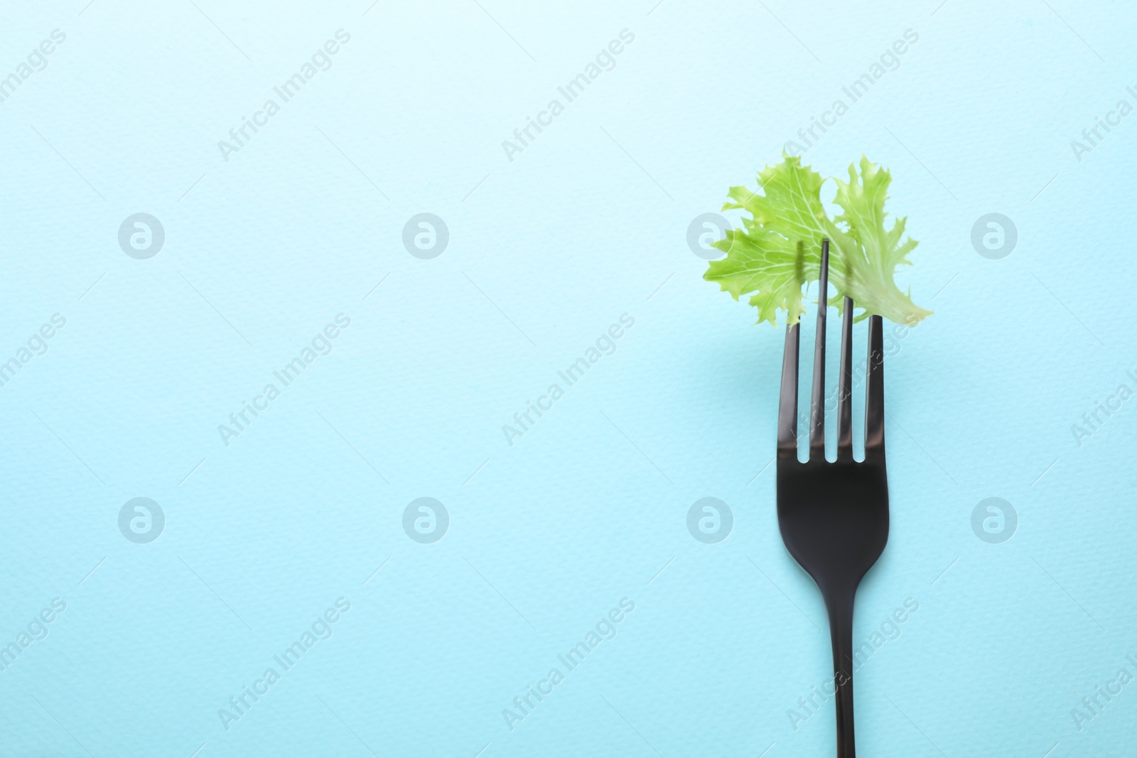 Photo of Fork with lettuce leaf on light blue background, top view and space for text. Diet concept