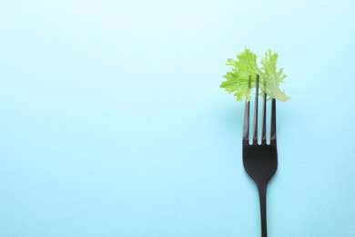 Fork with lettuce leaf on light blue background, top view and space for text. Diet concept