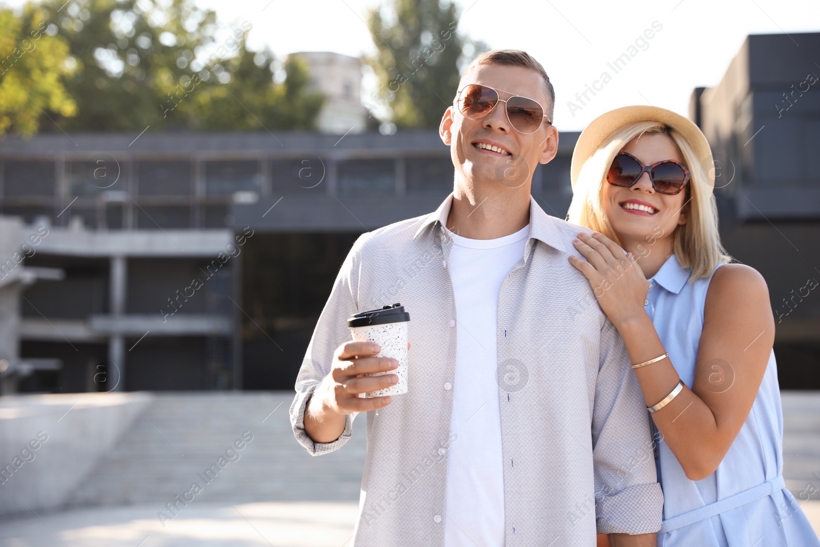 Photo of Happy couple with drink walking along city street on summer day