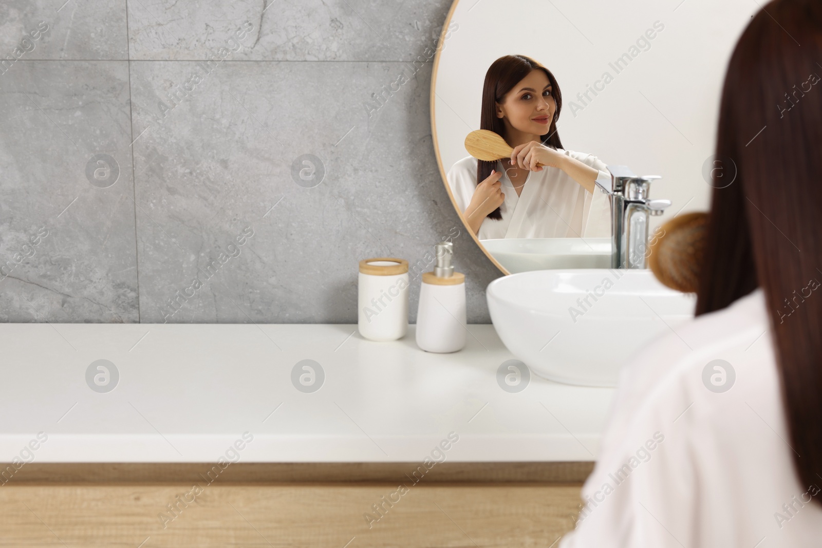 Photo of Beautiful woman brushing her hair near mirror in bathroom, space for text