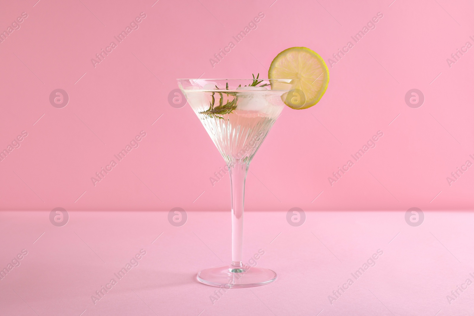 Photo of Martini glass of cocktail with lemon slice and rosemary on pink background