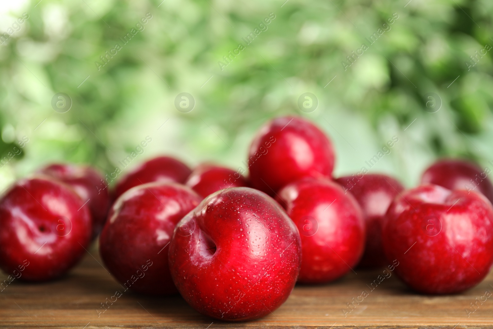 Photo of Delicious ripe plums on wooden table against blurred background, closeup. Space for text