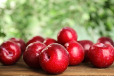 Photo of Delicious ripe plums on wooden table against blurred background, closeup. Space for text