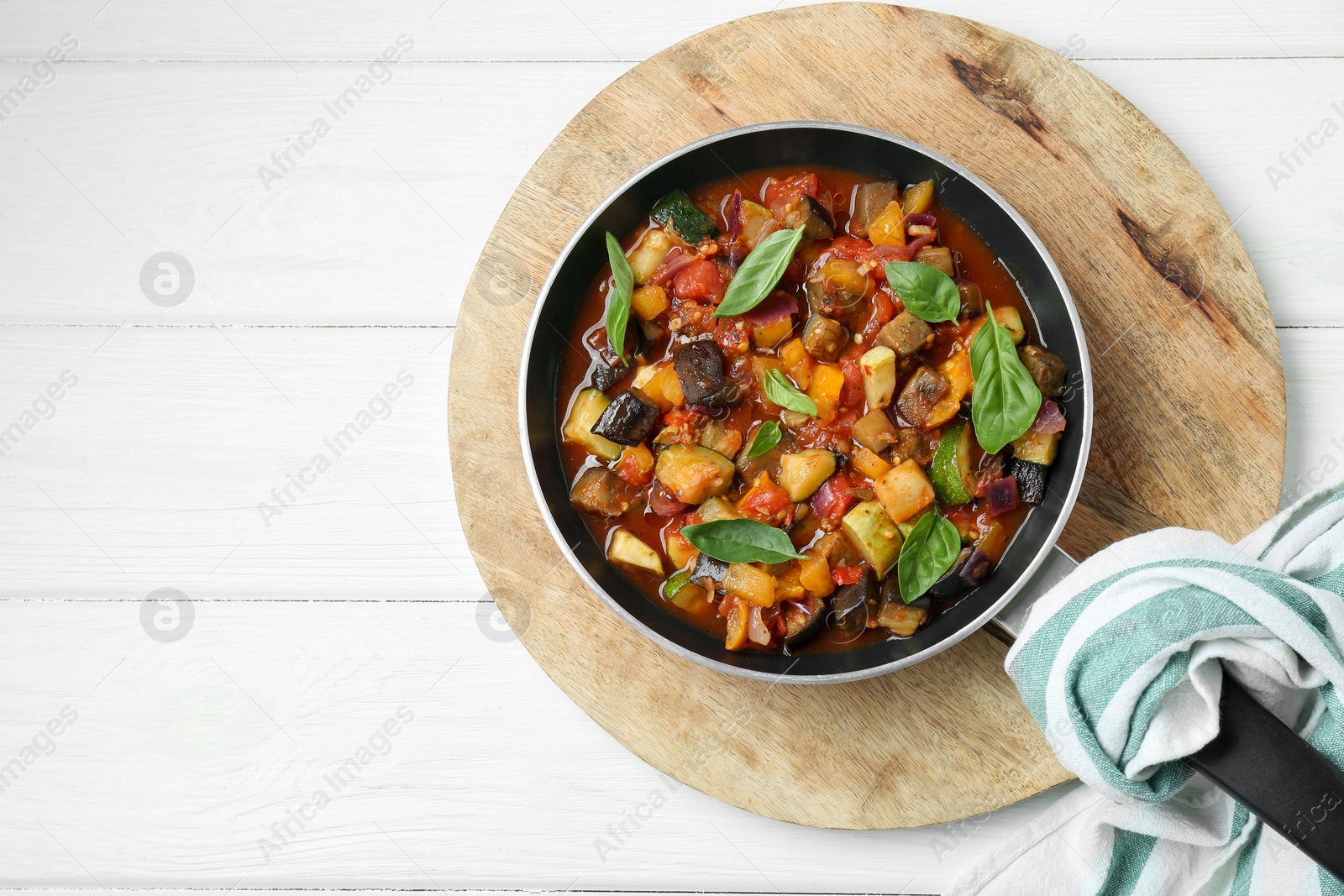 Photo of Frying pan with tasty ratatouille on white wooden table, top view. Space for text