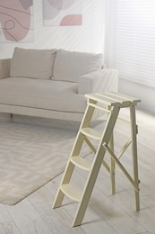 Photo of Folding ladder near sofa on wooden floor at home