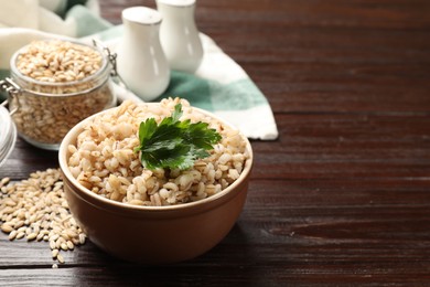 Photo of Delicious pearl barley with parsley in bowl on wooden table, space for text