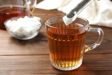 Adding sugar cube into cup of tea at wooden table, closeup