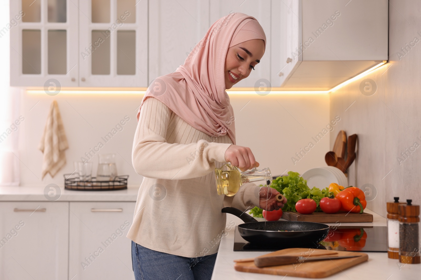 Photo of Muslim woman cooking delicious dish with vegetables on cooktop in kitchen
