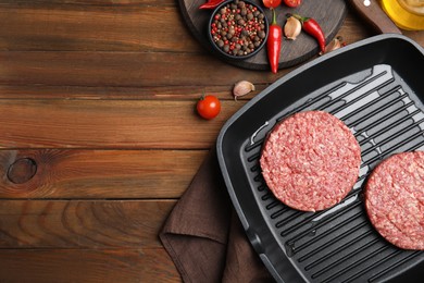 Raw hamburger patties with vegetables and pepper on wooden table, flat lay. Space for text