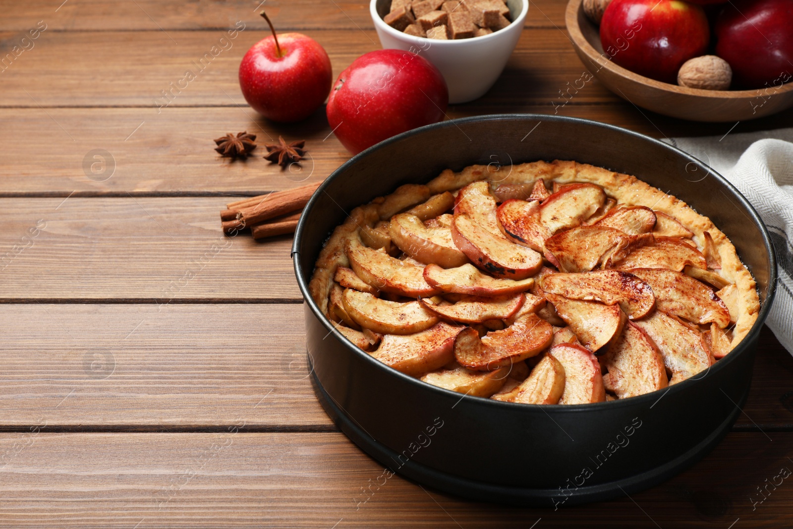 Photo of Delicious apple pie and ingredients on wooden table, space for text