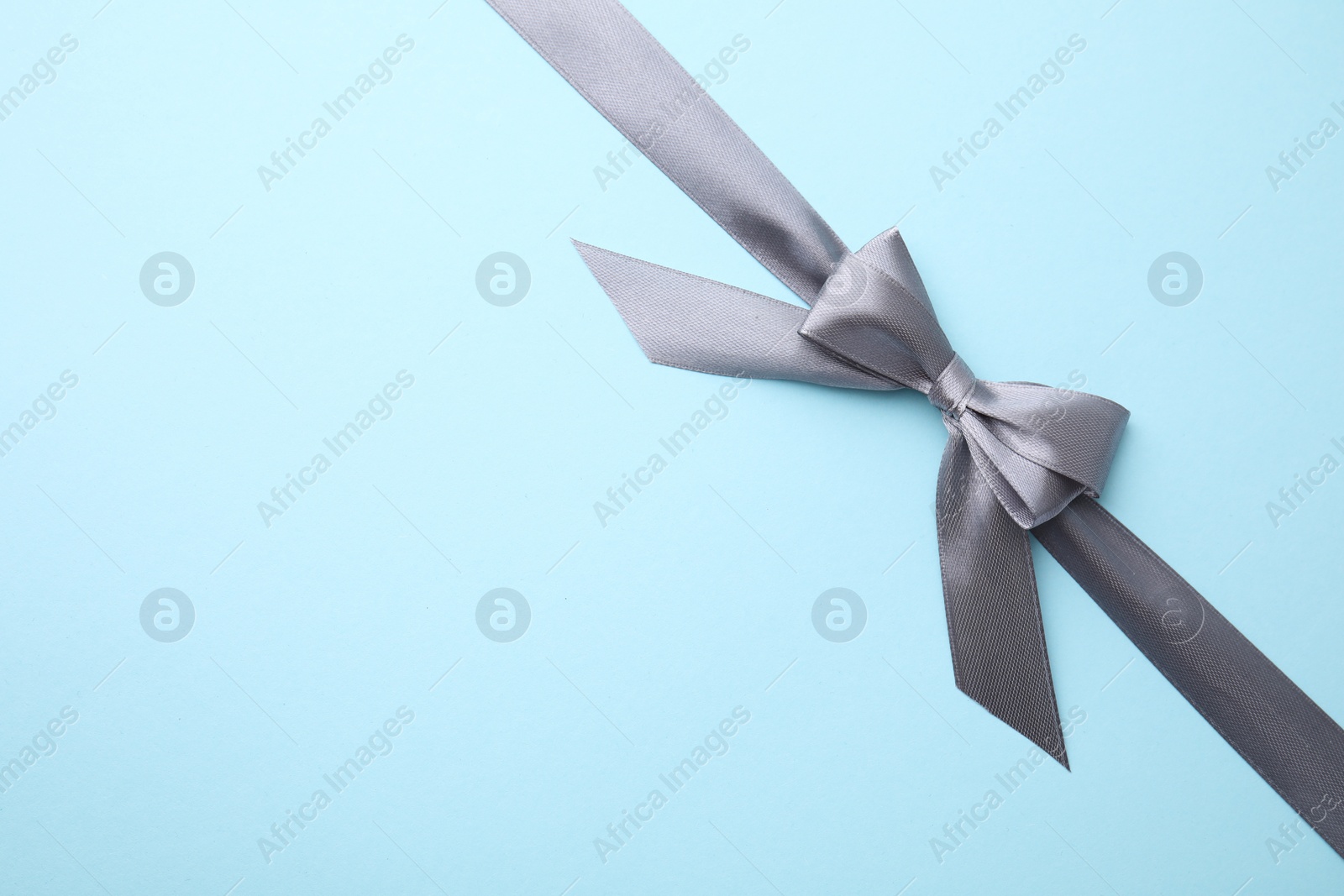 Photo of Grey satin ribbon with bow on light blue background, top view