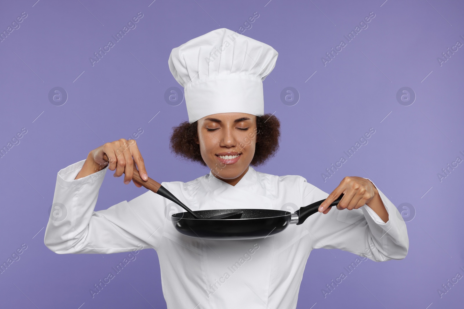 Photo of Happy female chef in uniform holding frying pan and ladle on purple background