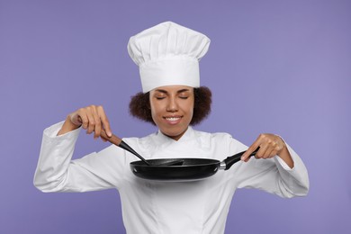 Happy female chef in uniform holding frying pan and ladle on purple background