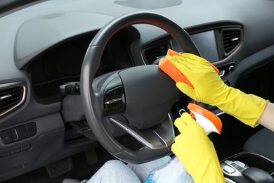 Woman cleaning steering wheel with rag in car, closeup