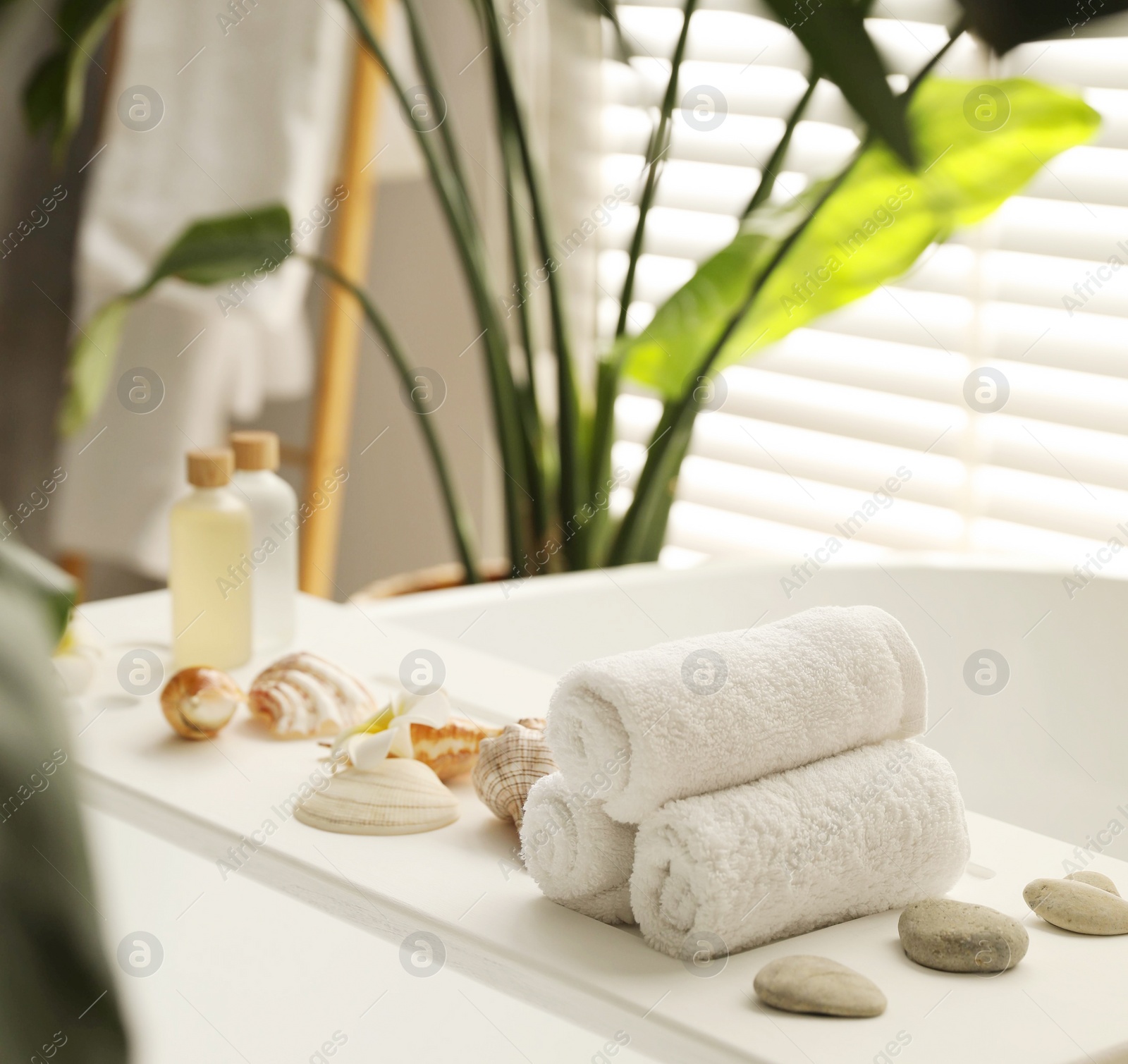 Photo of Bath tray with spa products, towels and shells on tub in bathroom